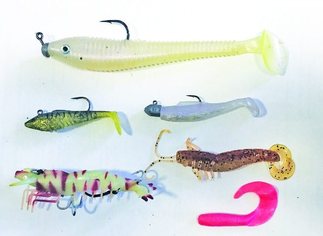 Soft plastic lures: Locally made Happy Rock Softies for big barra (top), pre-rigged Squidgy Slick Rig (top left), 3” Z-Man MinnowZ in Opening Night (top right), Prawnstar Gold Original in Lumo Tiger (bottom left), 4” Atomic Prong (mid right) and 4” Berkley Gulp Grub.